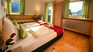 Ein Hotelzimmer mit zwei Betten, einem Holzkasten, einem Schreibtisch mit Lampe und Blick auf die Berge durch die Fenster.