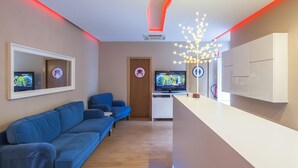 A modern hotel lobby with a blue sofa, a reception desk, and two televisions. - Vila Nova Guesthouse (Lisbon)