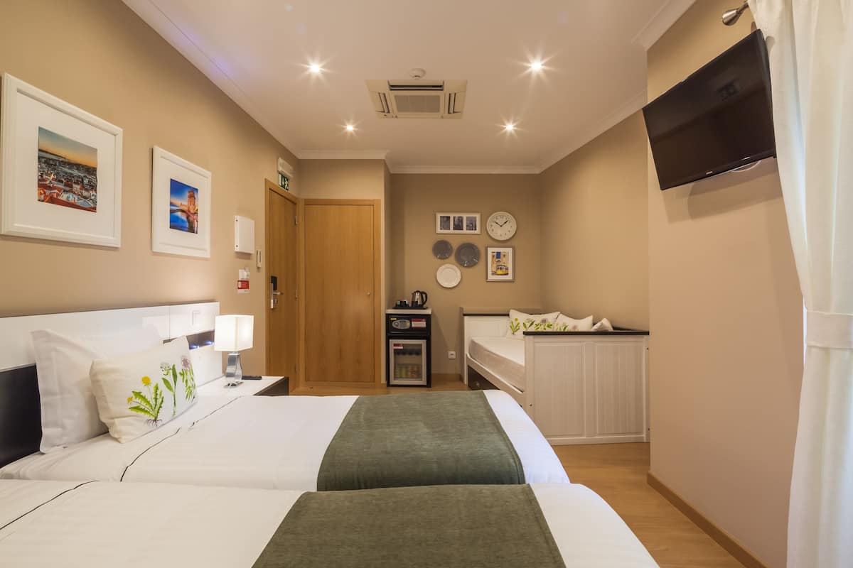A hotel room with two beds, a TV, a clock, and a small kitchenette.