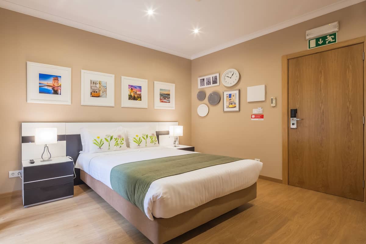 A hotel room with a bed, bedside tables, wall-mounted clocks, and framed pictures.
