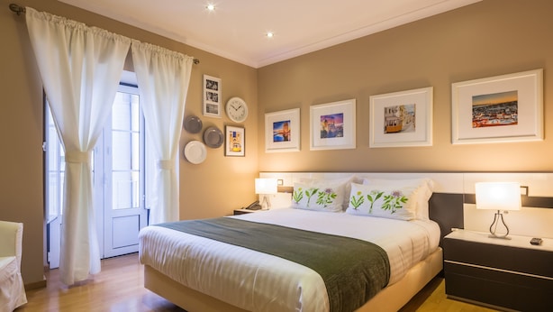 A neatly arranged bedroom with a large bed, bedside tables with lamps, a clock, and framed pictures on the wall. - Vila Nova Guesthouse (Lisbon)