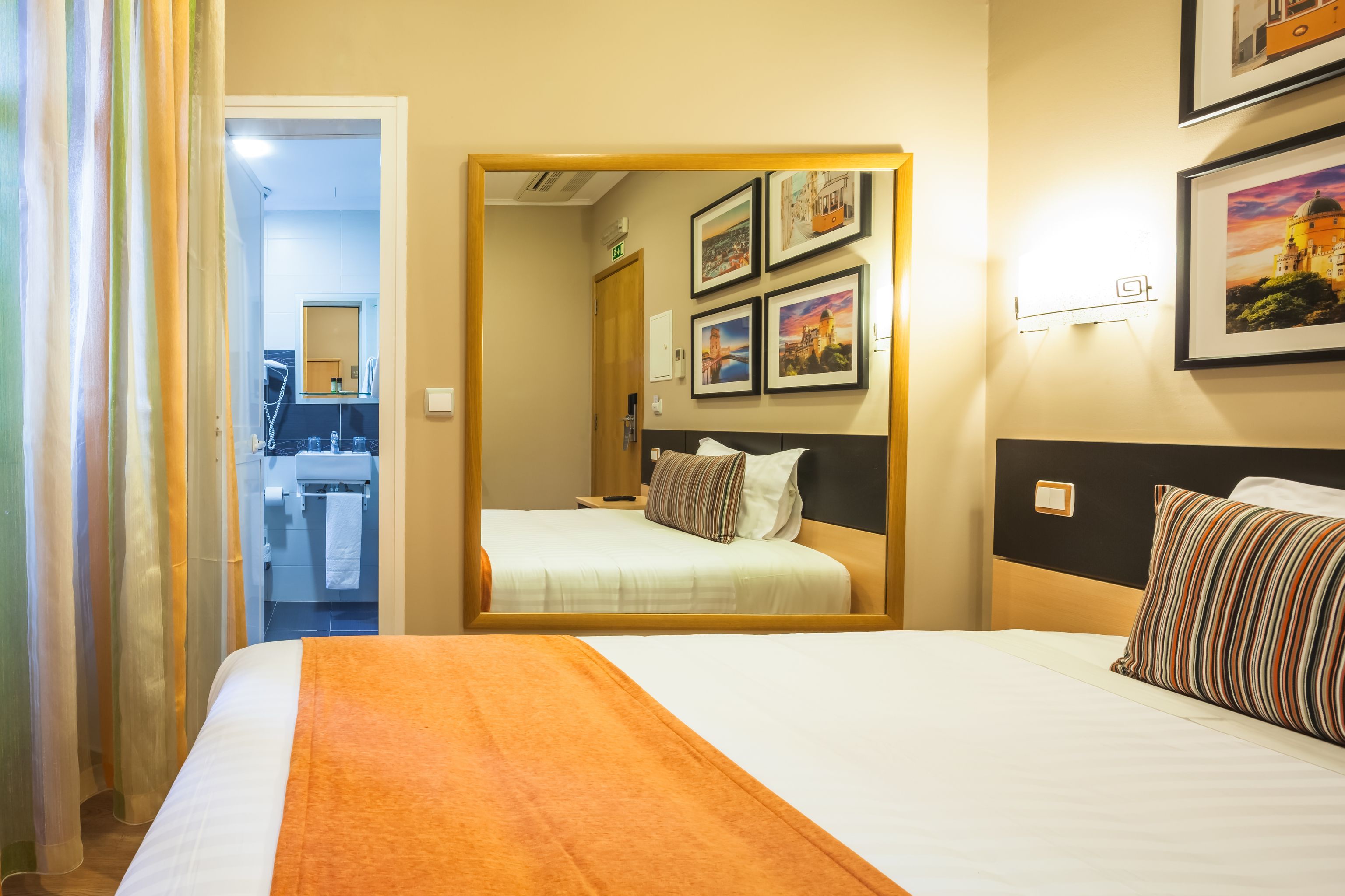 A hotel room with two beds, a bathroom visible through an open door, and framed pictures on the wall.