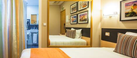 A hotel room with two beds, a bathroom visible through an open door, and framed pictures on the wall.