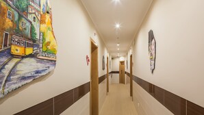 A hotel hallway with a mural of a tram and buildings on the left wall, wooden doors, and a tiled floor. - Vila Nova Guesthouse (Lisbon)