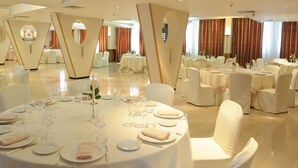 Un amplio salón de banquetes con mesas redondas dispuestas para el servicio de comidas, sillas blancas y elegantes centros de mesa.