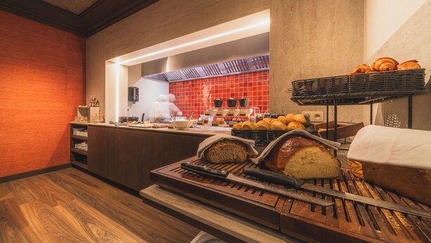 Ein reichhaltiges Frühstücksbuffet mit Brot, Gebäck und einem Koch, der Speisen zubereitet.