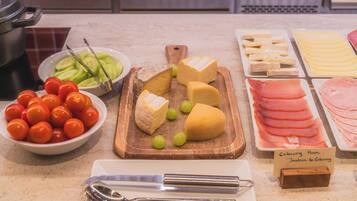 A variety of cheeses, tomatoes, and ham on a kitchen counter.
