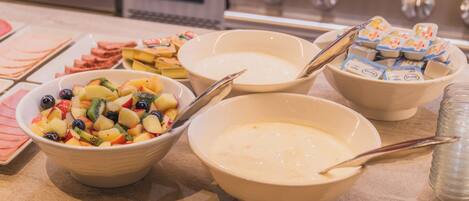 A buffet with bowls of fruit salad, yogurt, and other dishes.