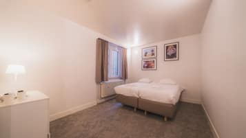 Una habitación pequeña y limpia con una cama, un escritorio, una lámpara, un radiador y tres cuadros en la pared.
