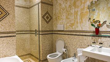 A bathroom with mosaic tile walls, a shower, a toilet, a bidet, and a sink with toiletries.