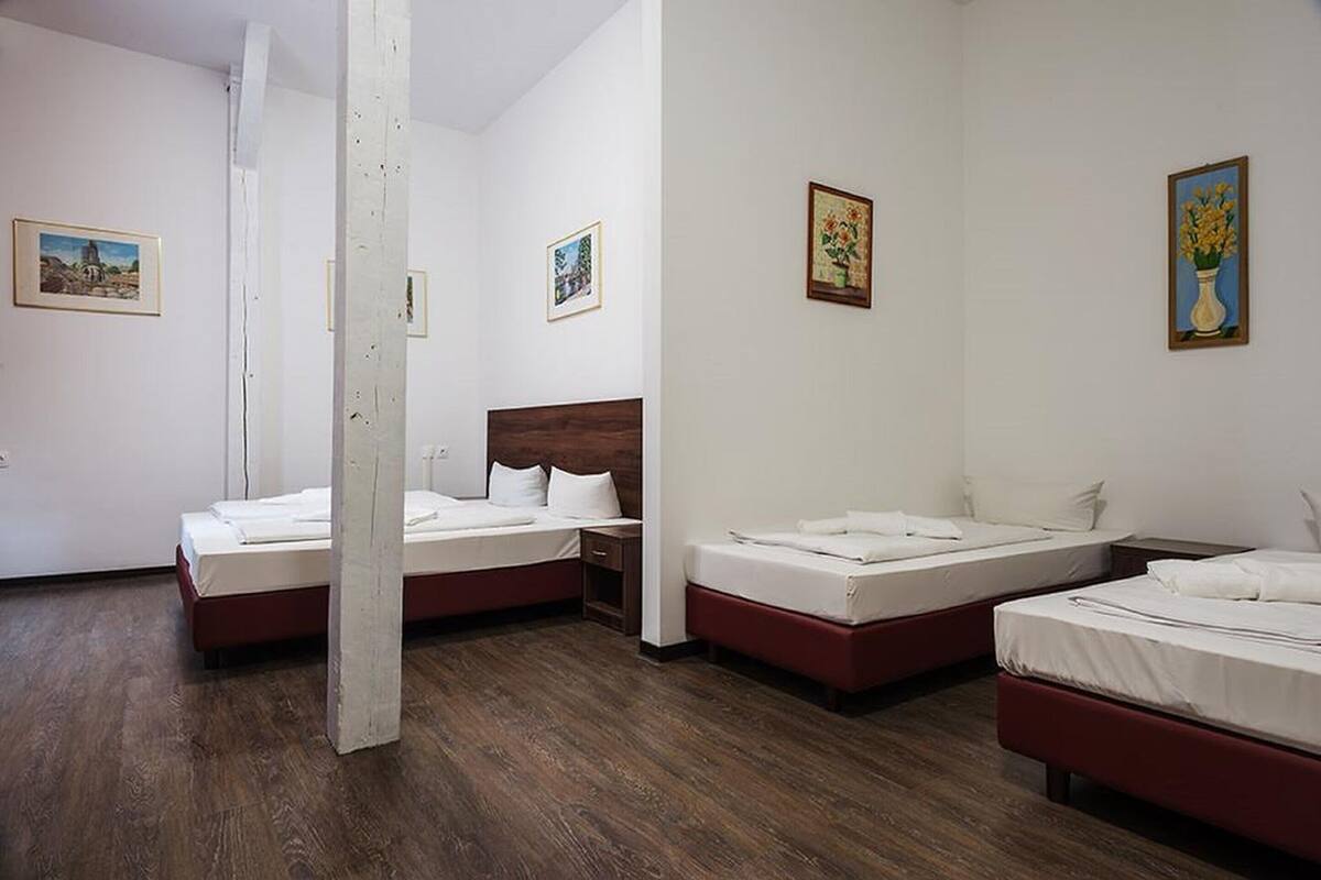Habitación de hotel con tres camas, paredes blancas y suelo de madera.