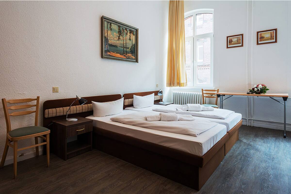 Habitación de hotel con una cama grande, un escritorio, una silla, una mesita de noche y una ventana con cortinas.