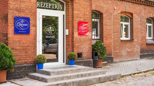 A brick building with a reception area, two potted plants, and a sign for Queen's Park. - Hotel Queenspark (Berlin)