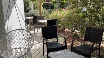 A wooden deck with outdoor furniture, including a hanging chair and two chairs, under a pergola with lanterns.