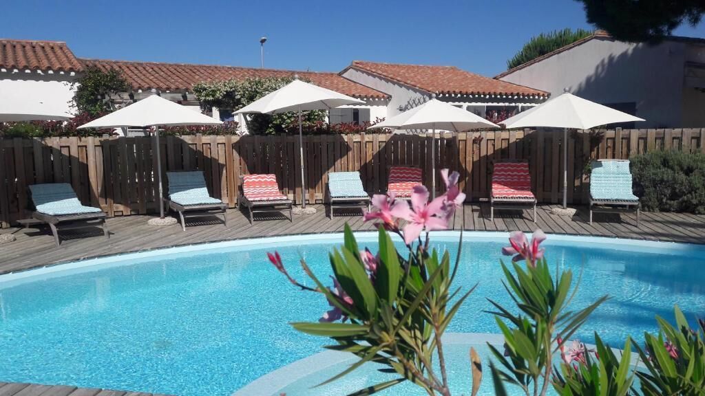 A swimming pool with lounge chairs and umbrellas, surrounded by a wooden deck and a fence.