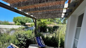 Eine Holzterrasse mit zwei gestreiften Liegestühlen und einem kleinen Tisch, unter einem Reetdach.