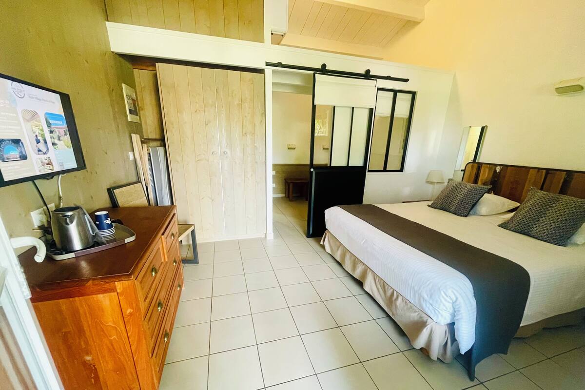 Une chambre d’hôtel avec un lit, une commode en bois, un bureau avec une bouilloire et un téléviseur fixé au mur.