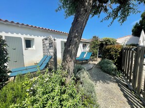 Uma área de pátio com duas espreguiçadeiras azuis, cerca de madeira e um pequeno jardim com diversas plantas.
