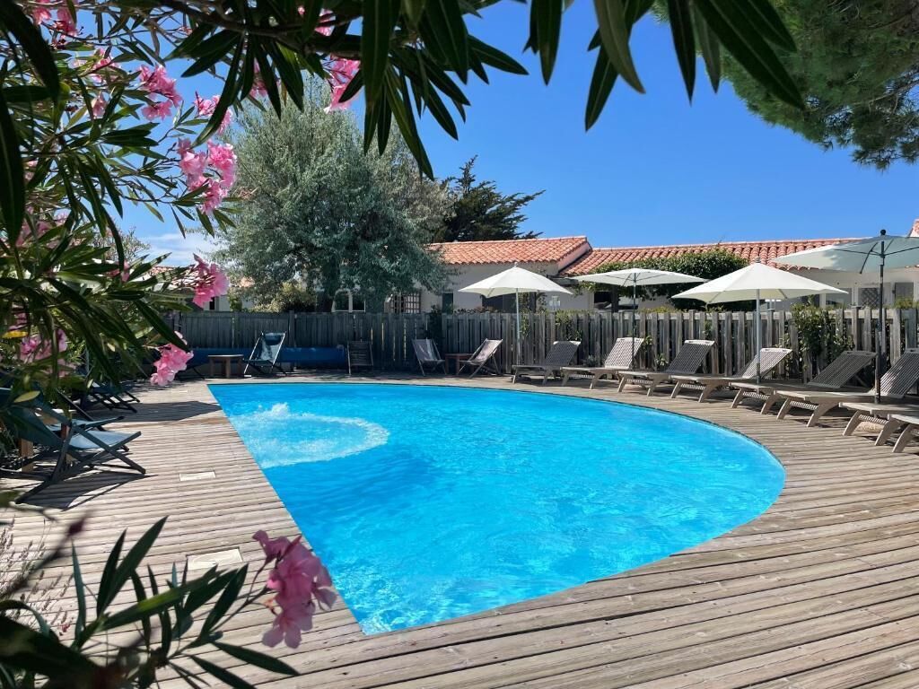 A swimming pool with a wooden deck, surrounded by lounge chairs and umbrellas.