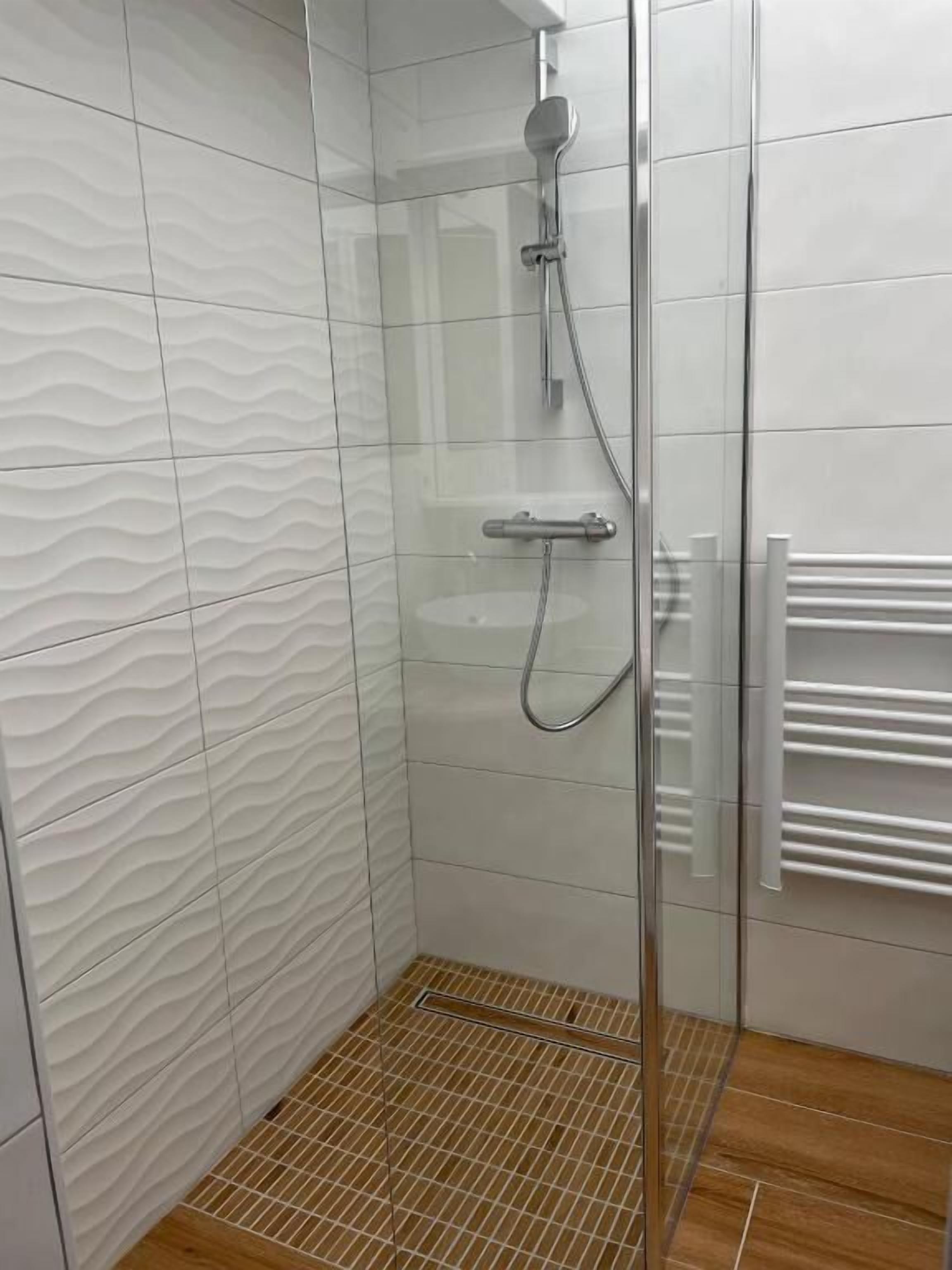 A shower area with a glass door, a showerhead, and a towel rack.