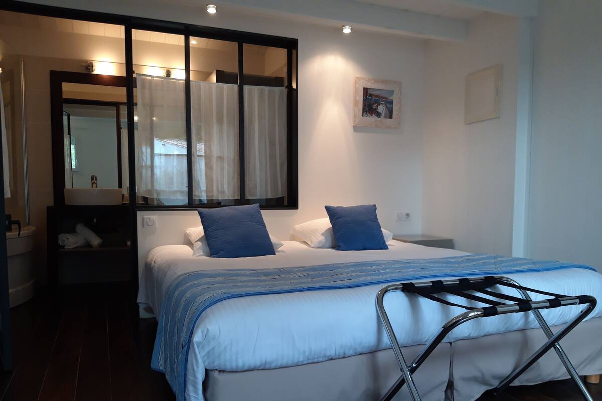 Une chambre à coucher moderne avec un grand lit, une table de chevet, un miroir et une fenêtre avec des rideaux.