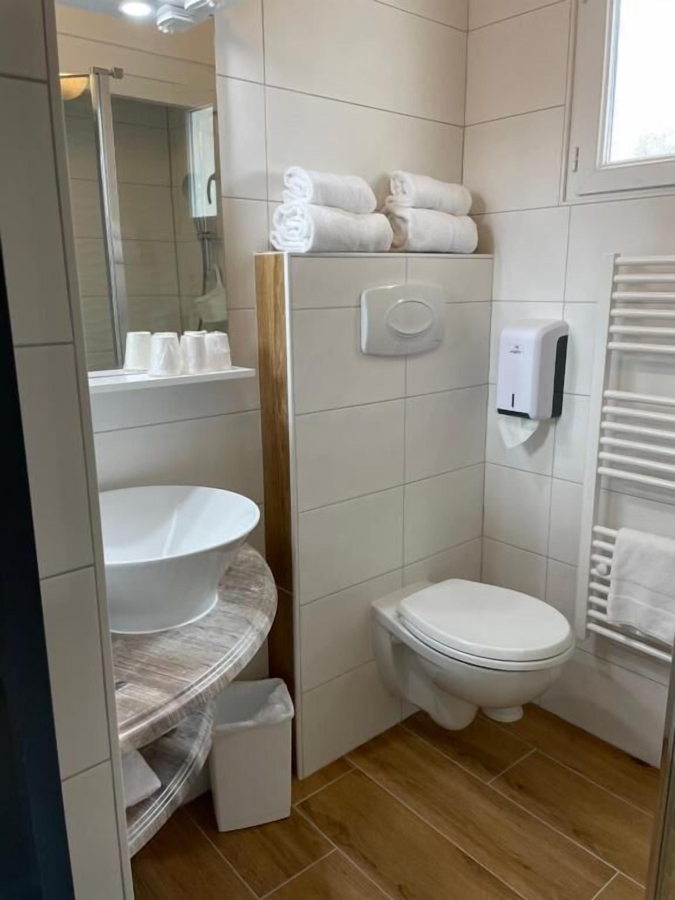 A bathroom with a toilet, sink, and shower. There are towels and a hand dryer.
