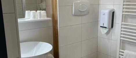 A bathroom with a toilet, sink, and shower. There are towels and a hand dryer.