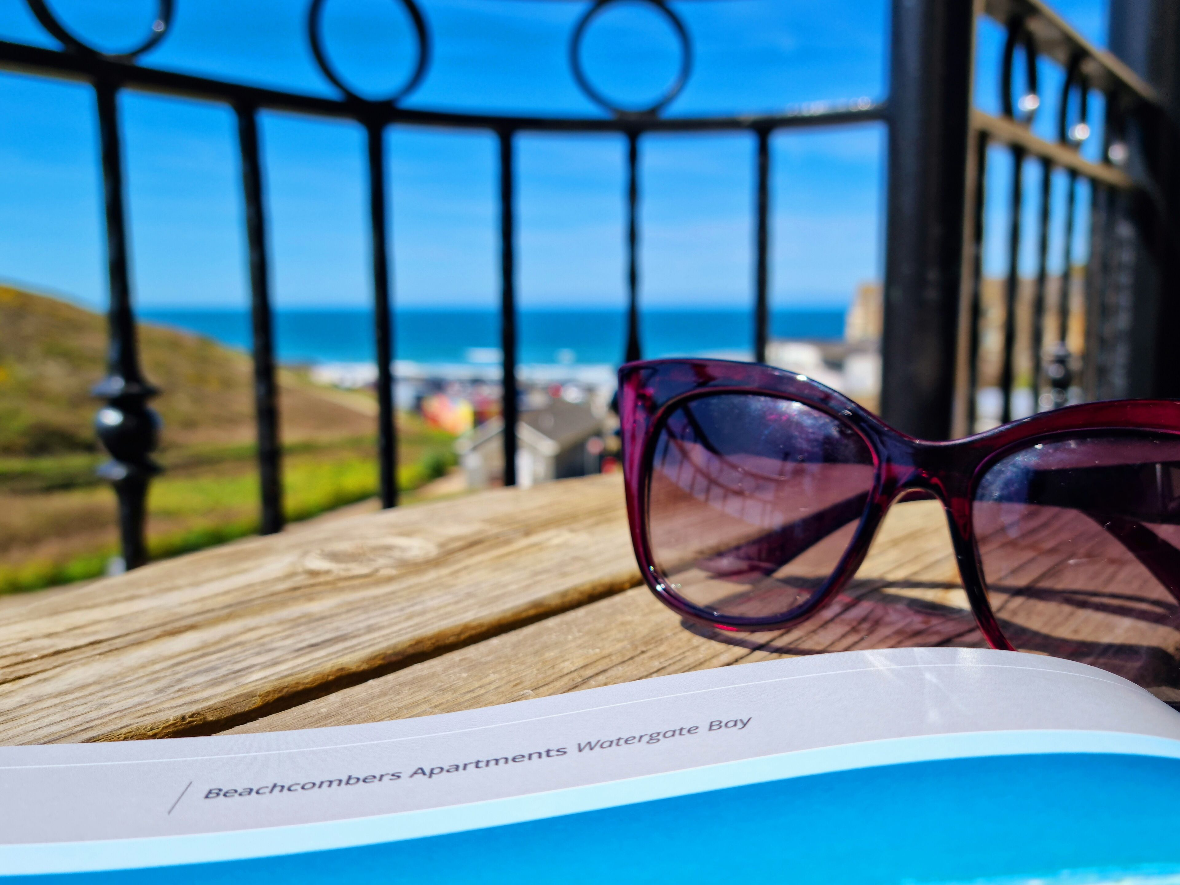 A pair of sunglasses on a wooden surface with a brochure titled "Beachcombers Apartments Watergate Bay".