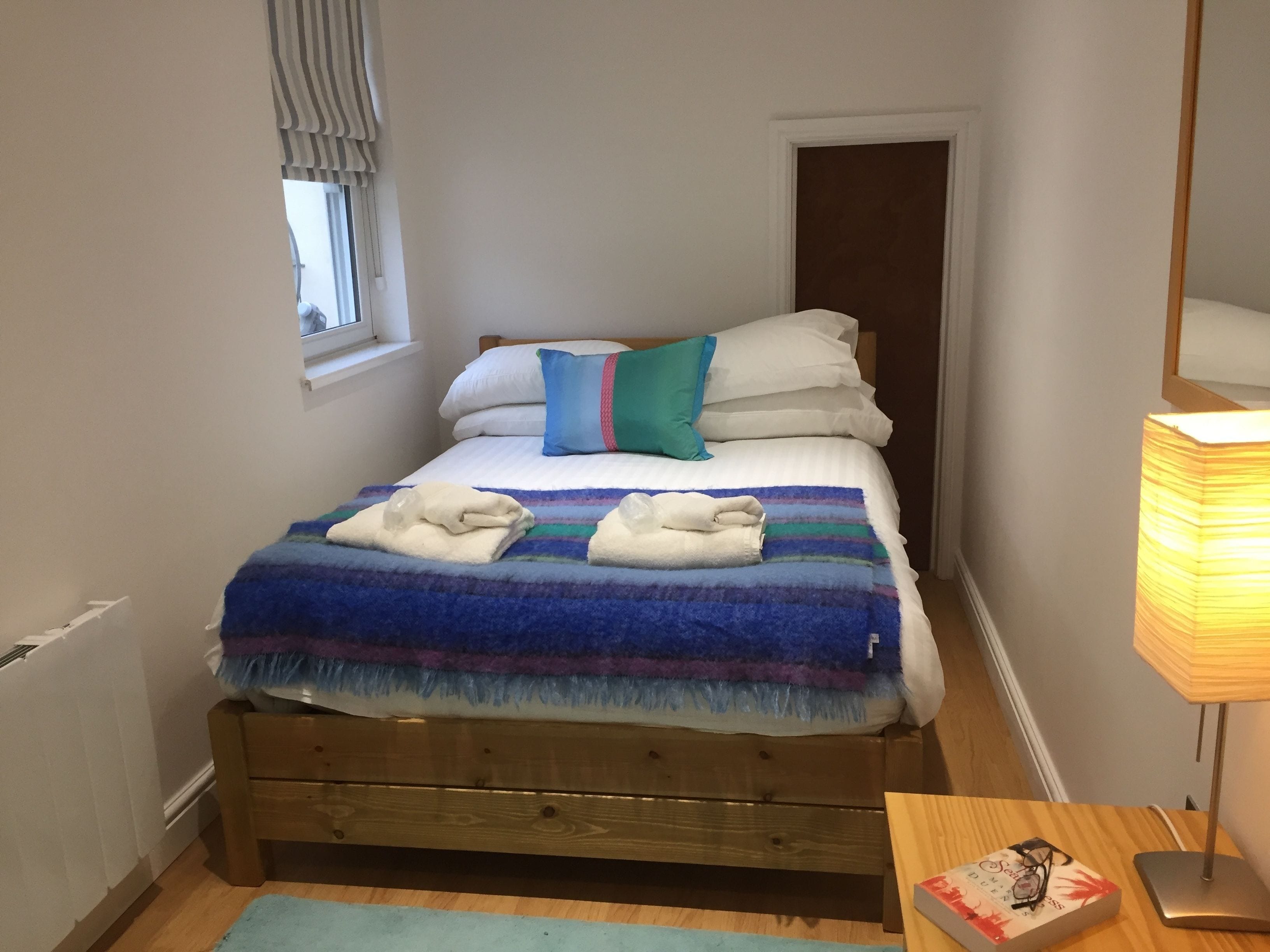 A bed with a blue and purple blanket, white pillows, and a teal pillow. There are two towels on the bed.