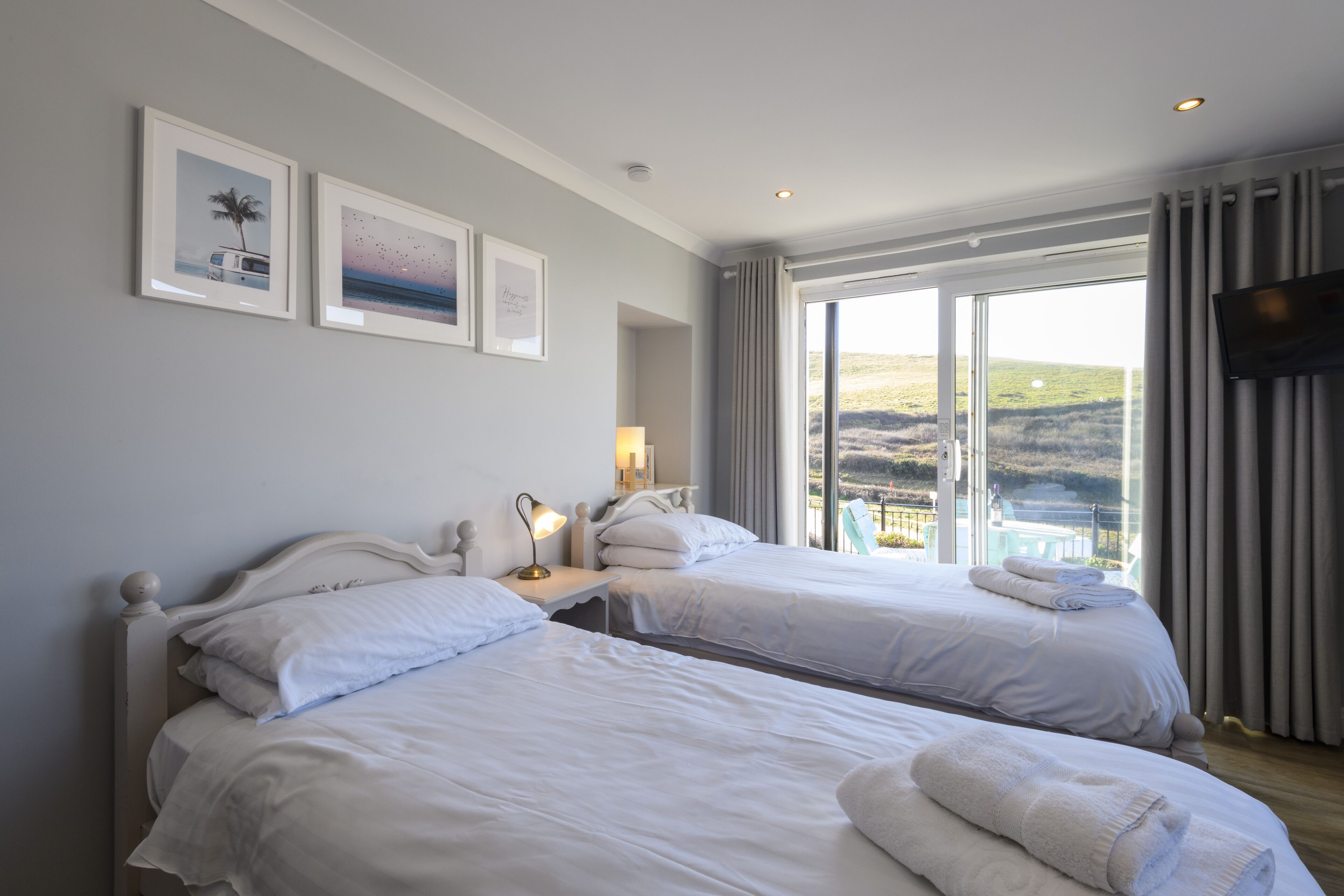 A hotel room with two beds, a TV, and a balcony with a scenic view.