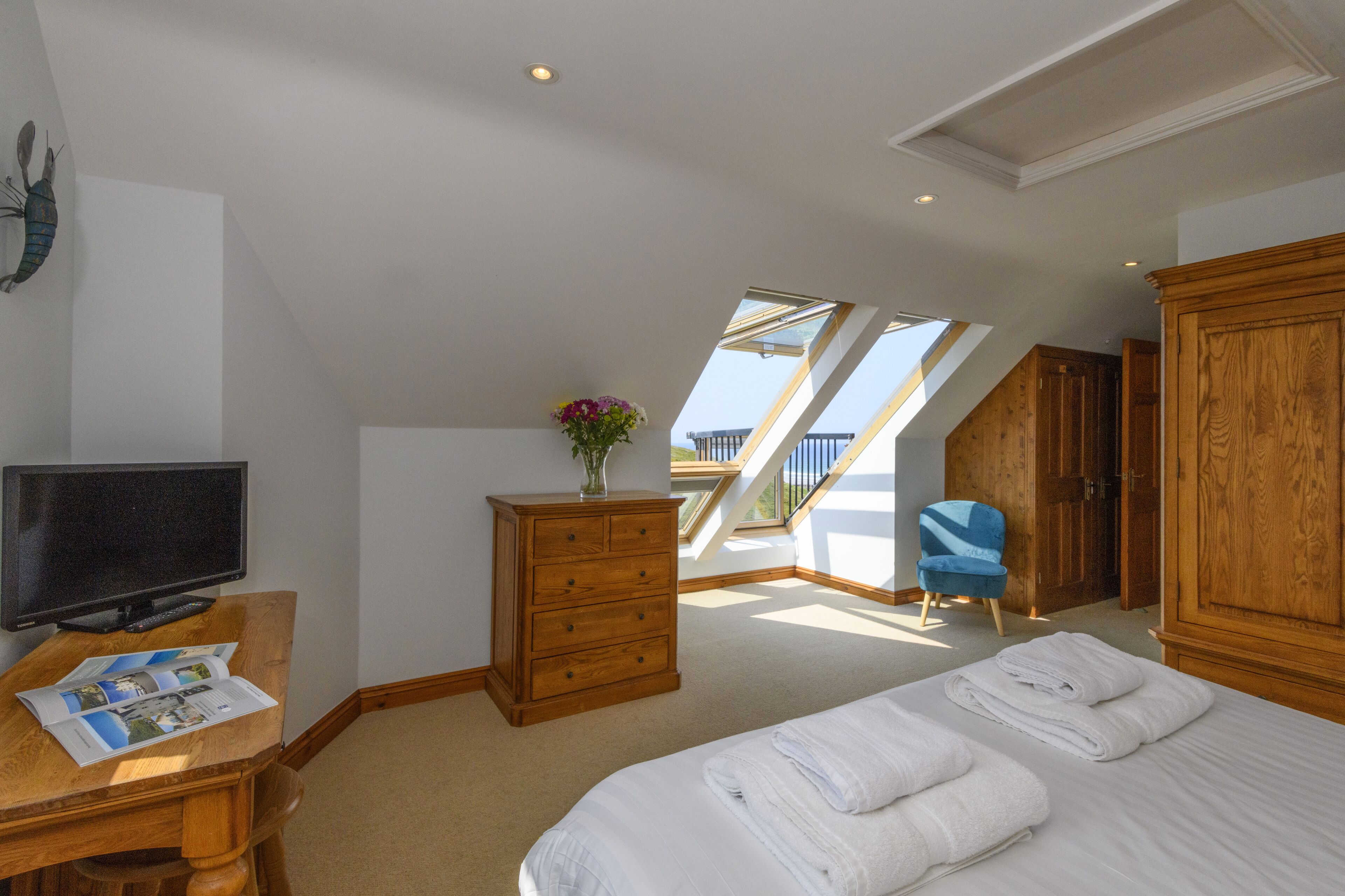 A bedroom with a bed, a dresser, a television, and a skylight.