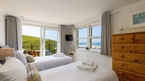 A hotel room with two beds, a wooden dresser, a TV, and a balcony with a view of the sea. - Beachcombers Apartments (Newquay)