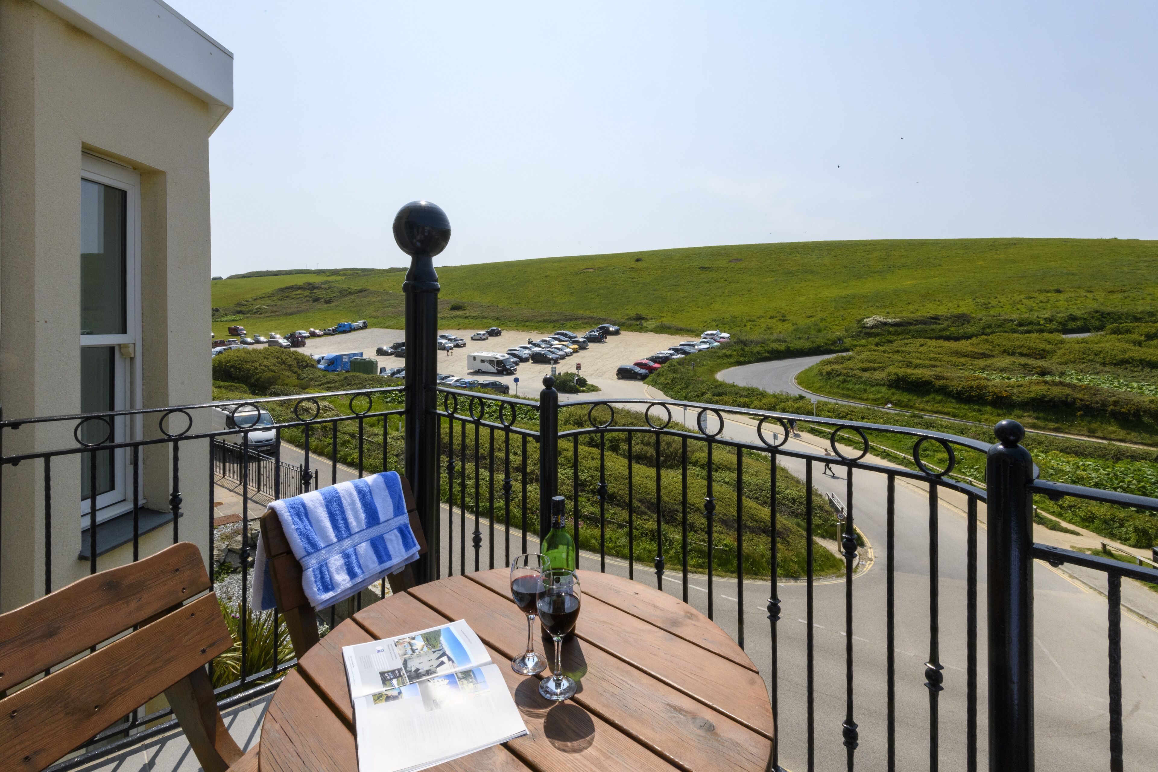 A balcony with a wooden table, a bench, and a view of a parking lot and green landscape.