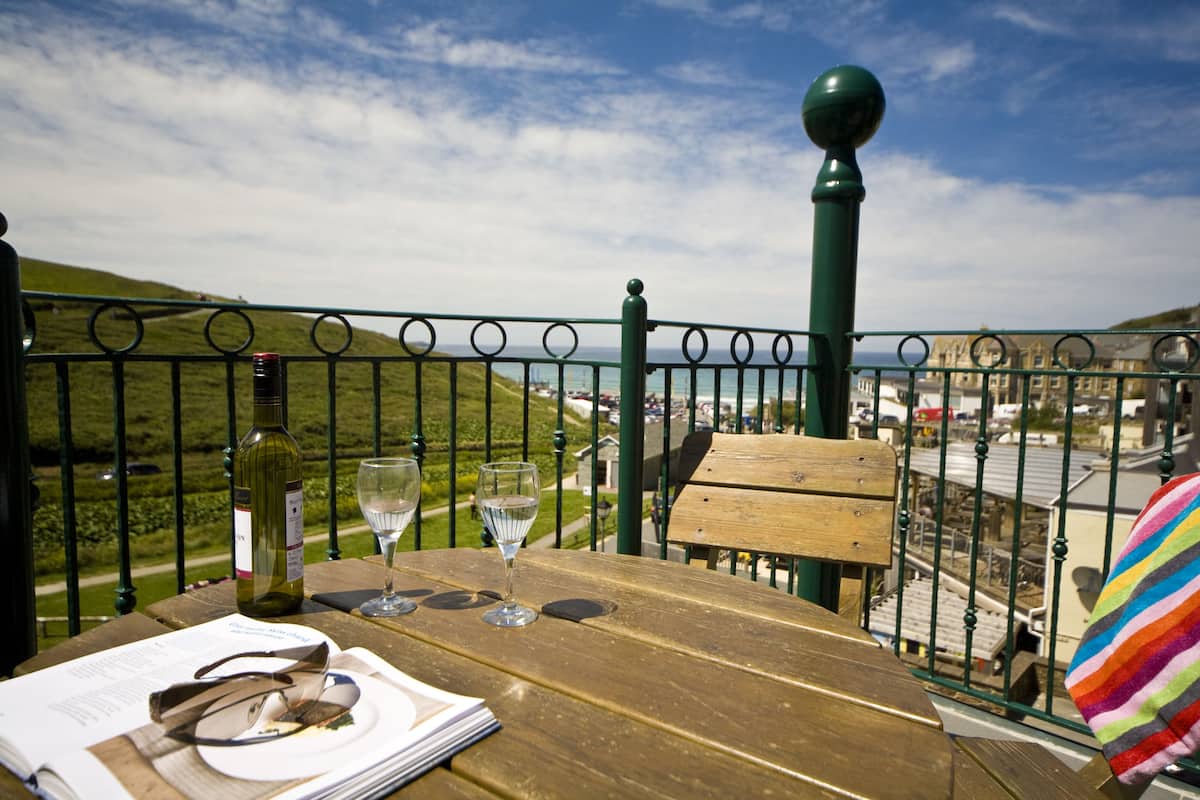 Una mesa de madera con una botella de vino, dos copas y un menú en un balcón con vista al litoral.