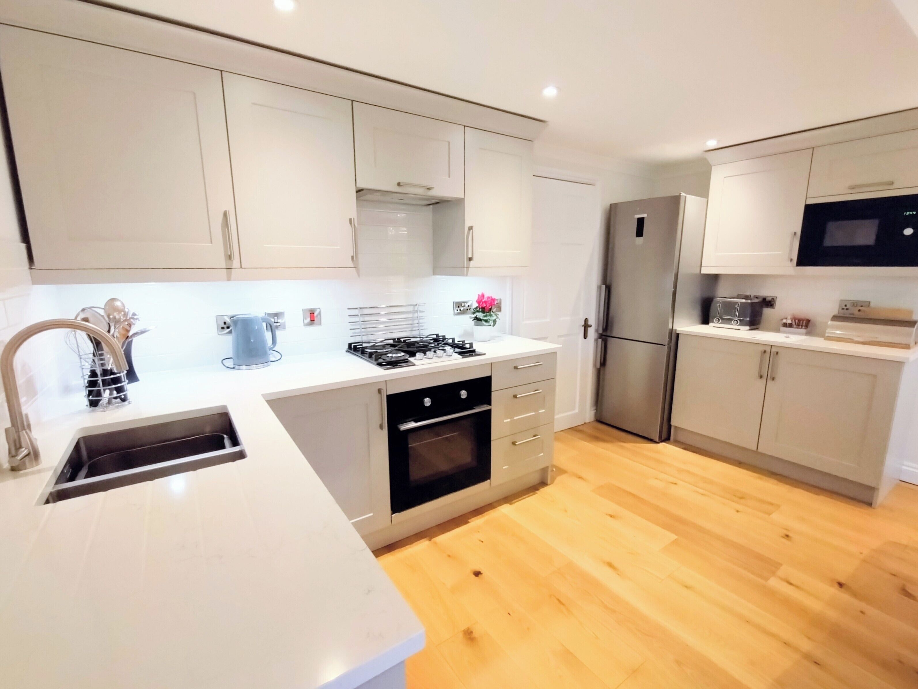 A modern kitchen with white cabinets, a stainless steel refrigerator, a microwave, and a gas stove.