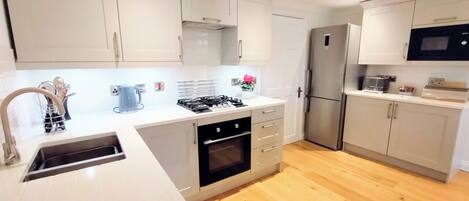 Una cocina moderna con gabinetes blancos, un refrigerador de acero inoxidable, un microondas y una estufa a gas.