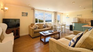 A living room with a sofa, a coffee table, a TV, and a dining area with a table and chairs. - Beachcombers Apartments (Newquay)