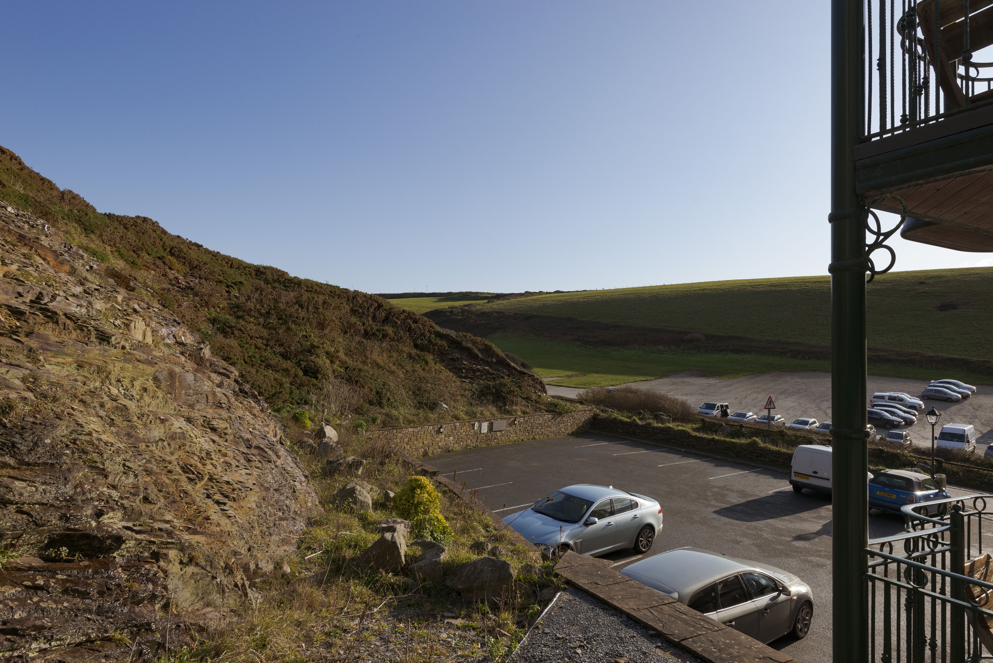 A parking area with cars and a van, surrounded by a hilly landscape.