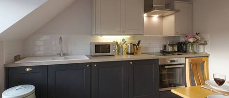 Une cuisine moderne avec des meubles de couleur sombre, un four à micro-ondes, un four traditionnel et un évier.