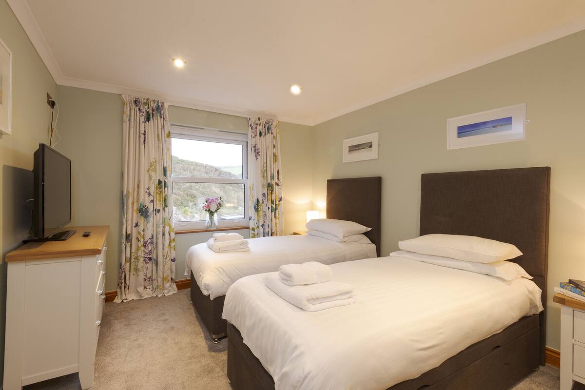 Una habitación de hotel con dos camas, televisión, ventana con cortinas y un pequeño escritorio.