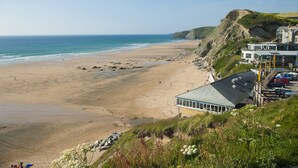 A coastal hotel with a beach view, a parking area, and a building with a green roof. - Beachcombers Apartments (Newquay)