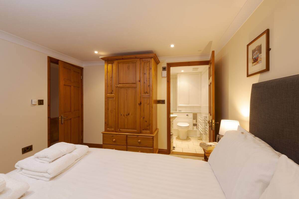 Una habitación de hotel con una cama grande, un armario de madera y un baño con inodoro y lavabo.