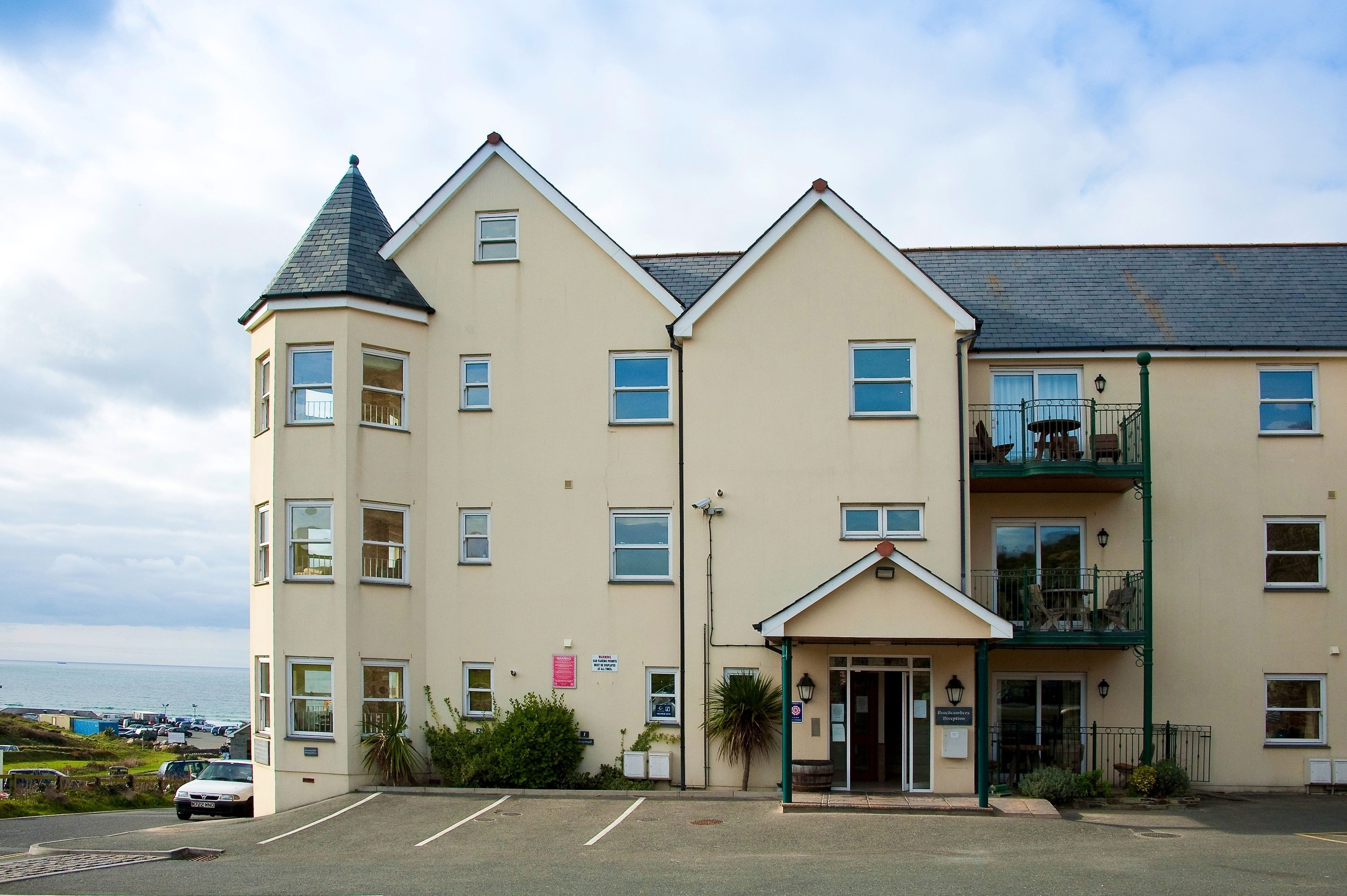 A two-story building with a flat roof, a corner turret, and a balcony on the second floor. There is a sign indicating the building is a hotel.