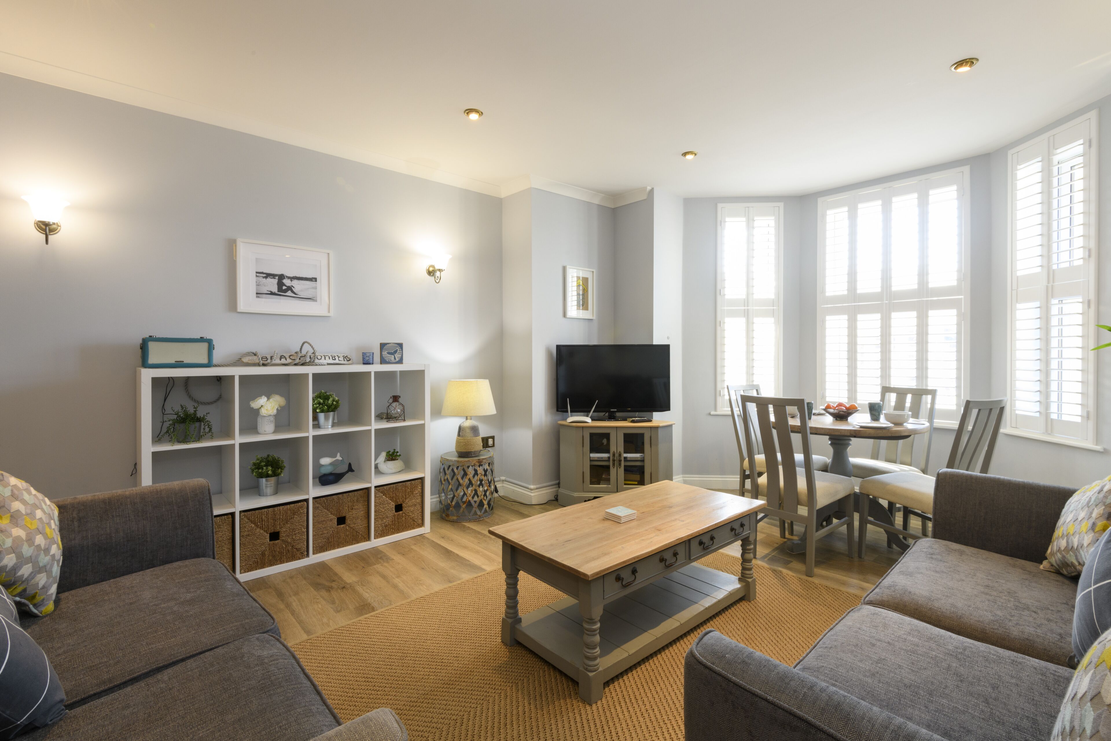 A modern living room with a sofa set, a coffee table, a TV, and a dining area with chairs and a table.