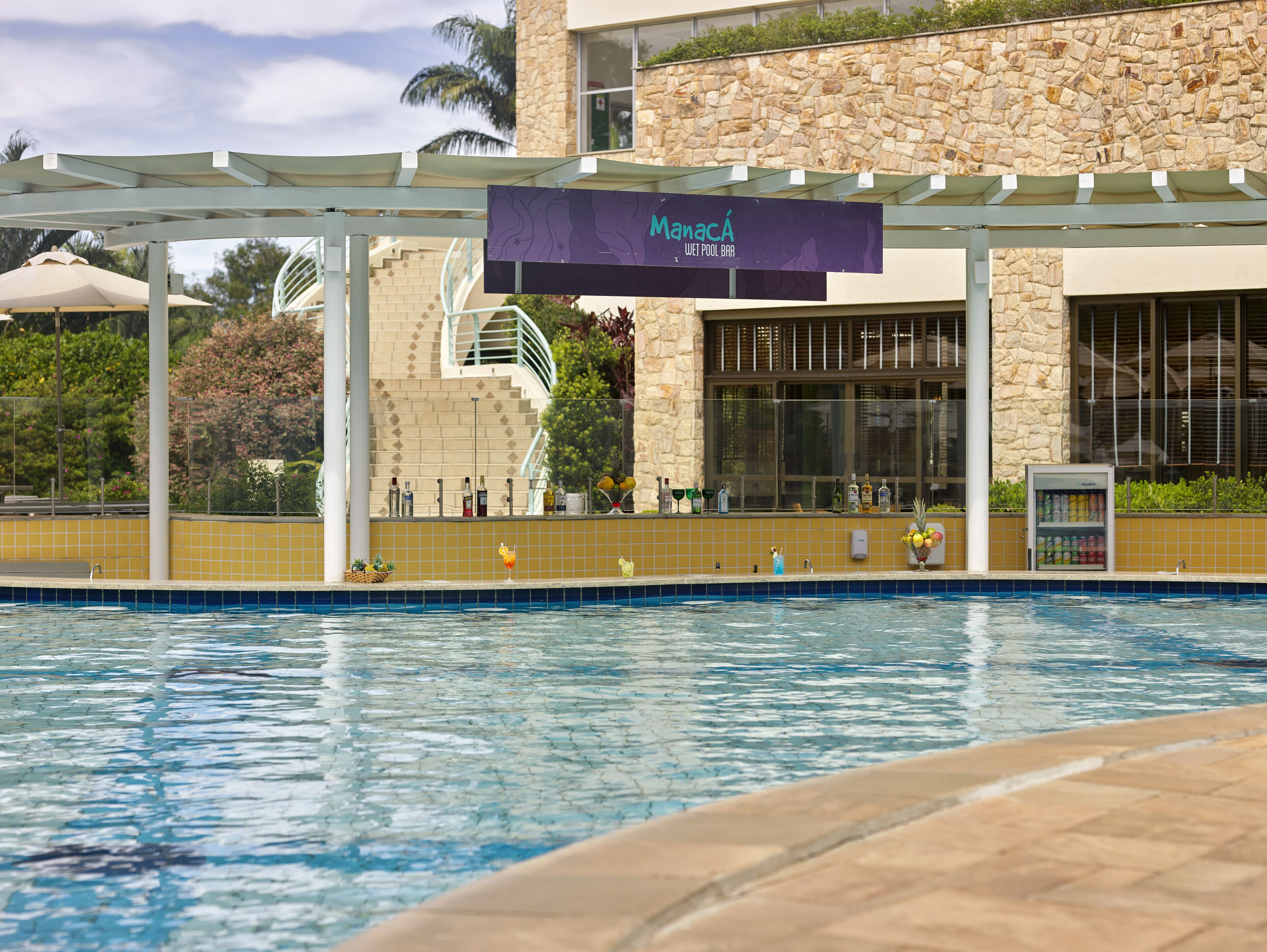 A pool area with a sign for Manaca Wet Pool Bar, a stone building, and a tiled pool edge.