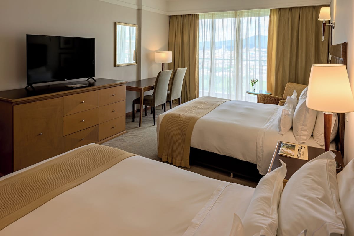 A hotel room with two beds, a TV, a desk, and a chair.