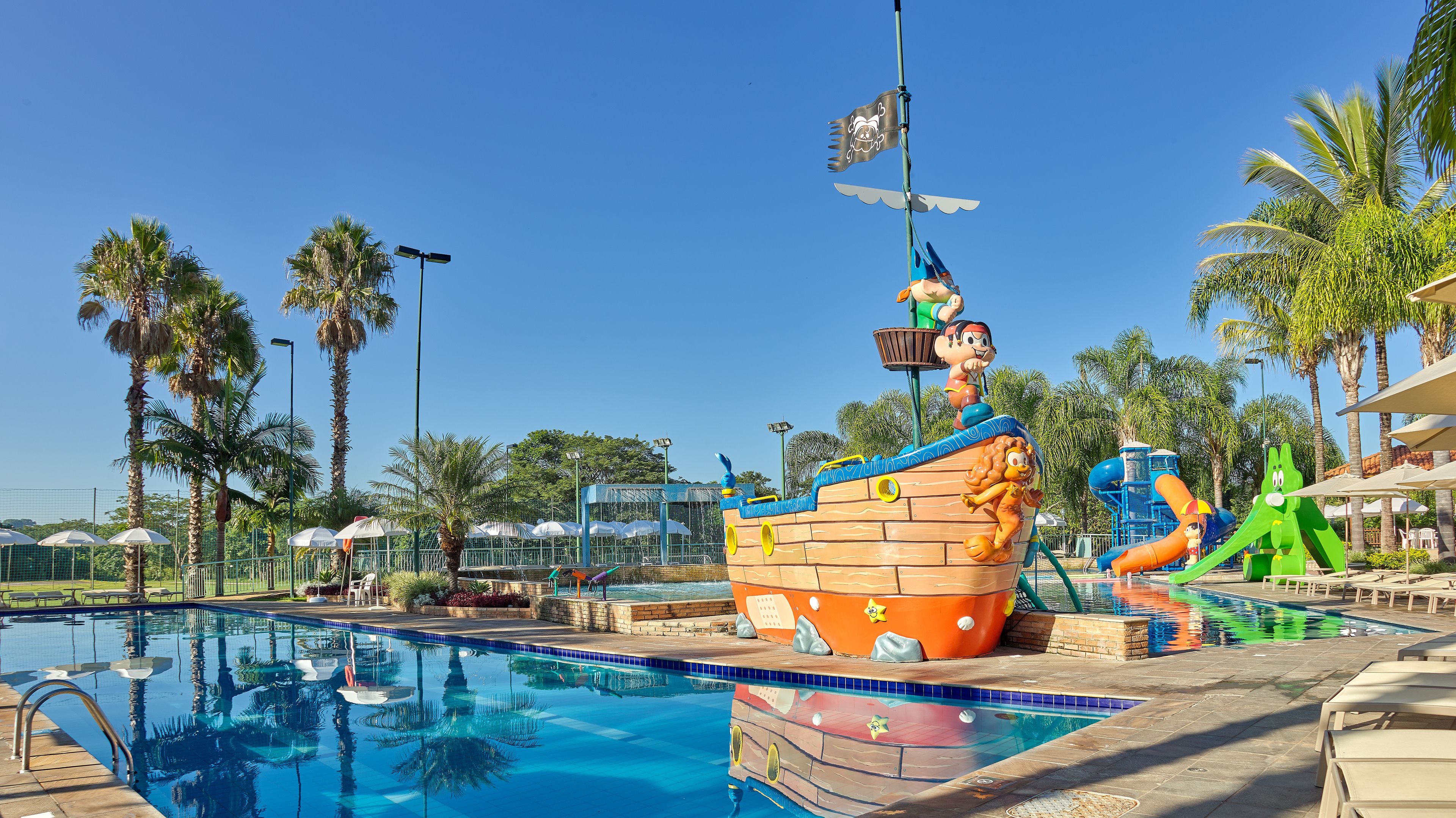 Uma piscina com decoração de navio pirata, palmeiras e um escorregador.