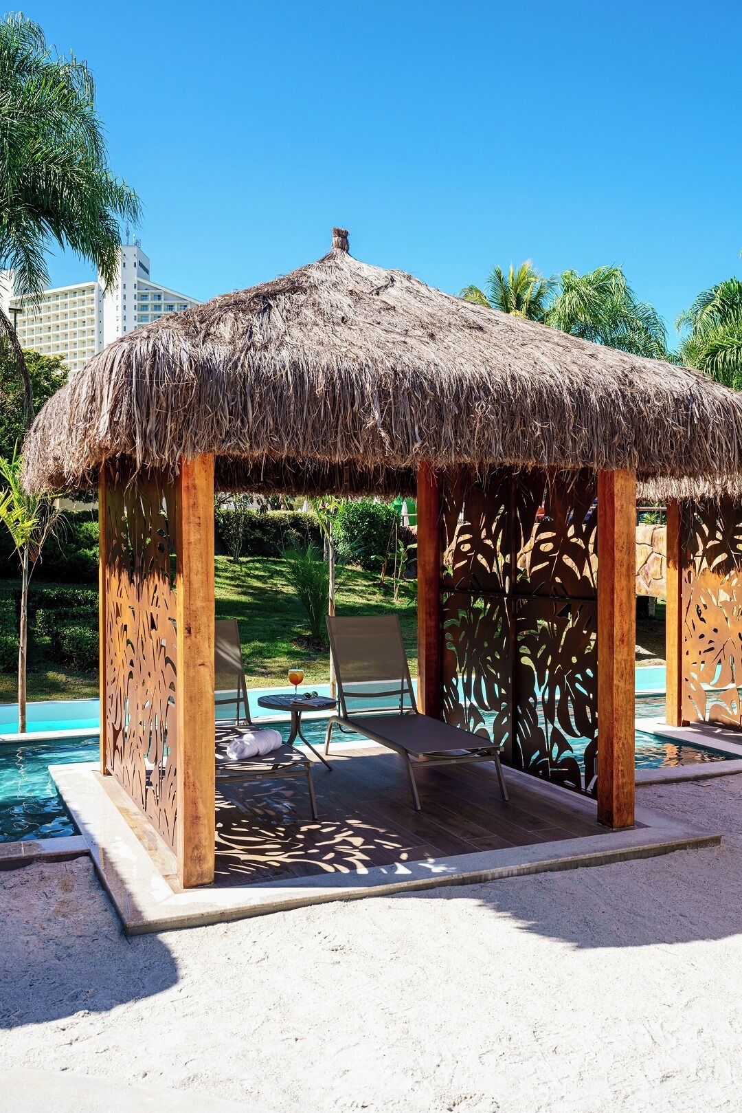 A thatched-roof gazebo with a pool in the background.
