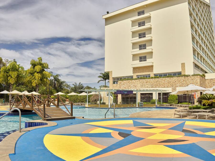 Uma área de piscina de hotel com uma piscina grande, um deck de madeira e um edifício com vários andares e varandas.