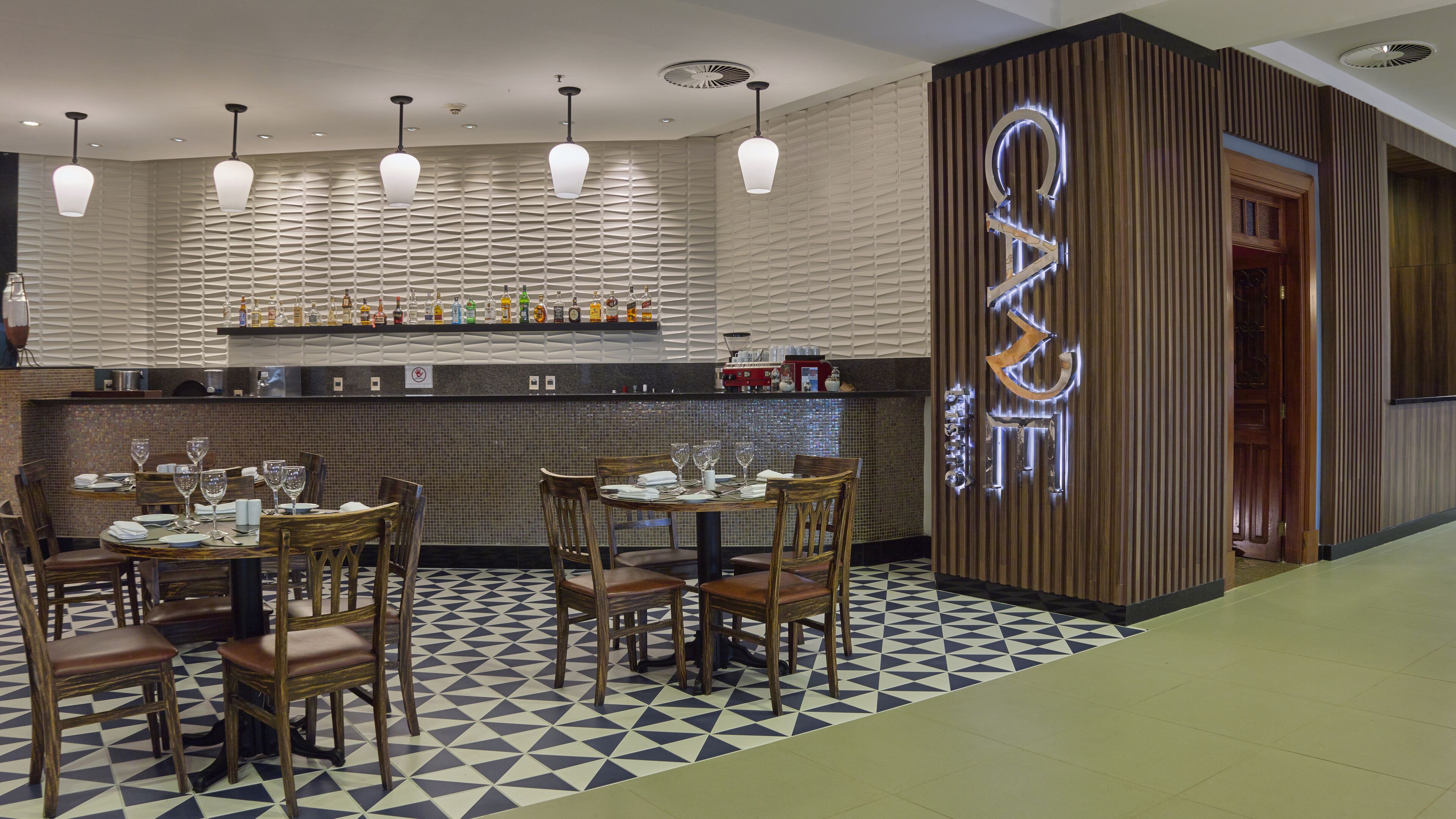 A restaurant with a bar area, wooden chairs, and a patterned floor.